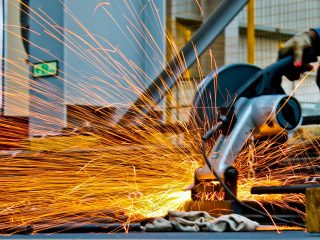 A worker operates a grinder cutting metal, creating a vibrant display of sparks in an industrial setting.