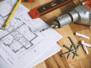 Close-up of construction blueprint with tools like drill and screws on a wooden table.